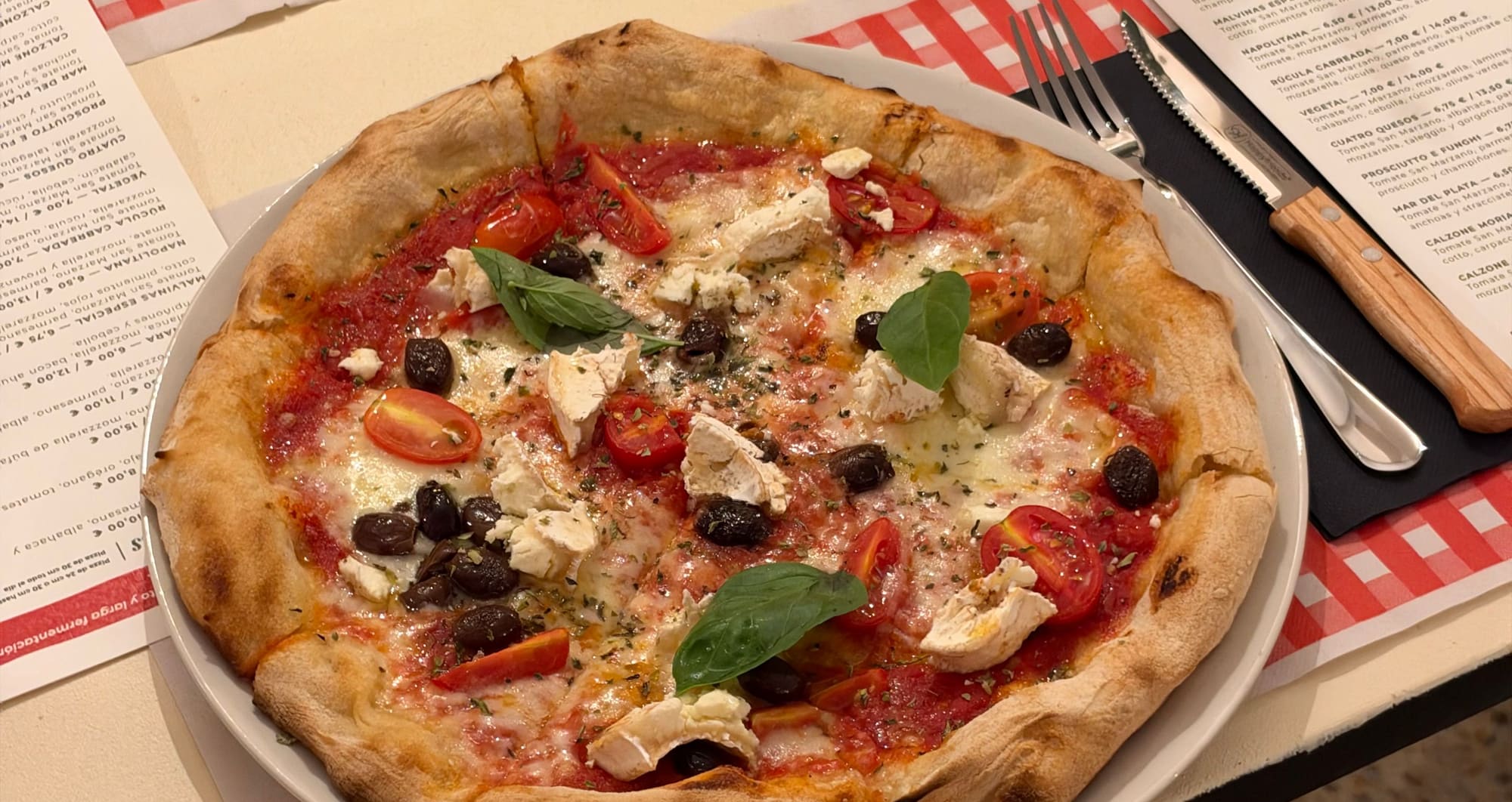 Pizza con tomate San Marzano, mozzarella, queso de cabra y olivas sobre un mantel de cuadros rojos
